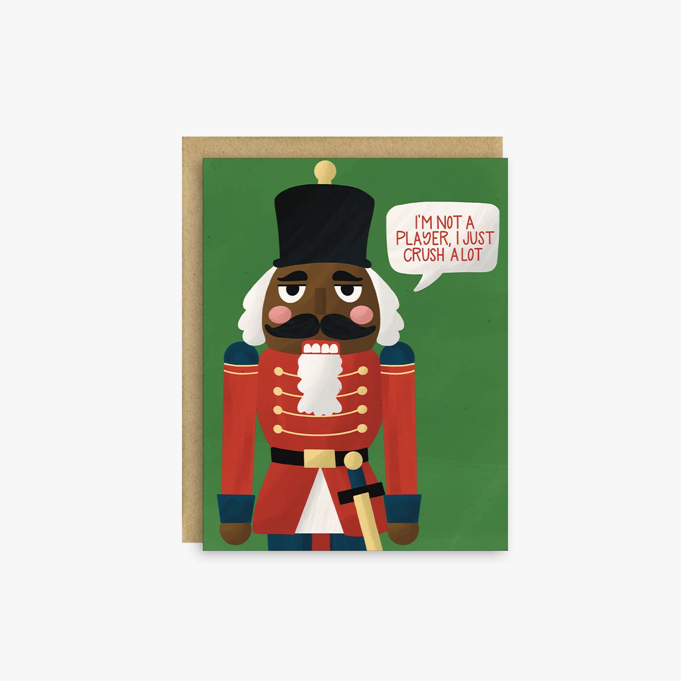 A greeting card featuring a stylized nutcracker character on a green background, with a kraft envelope behind it. The speech bubble reads, 'I'M NOT A PLAYER, I JUST CRUSH ALOT'.