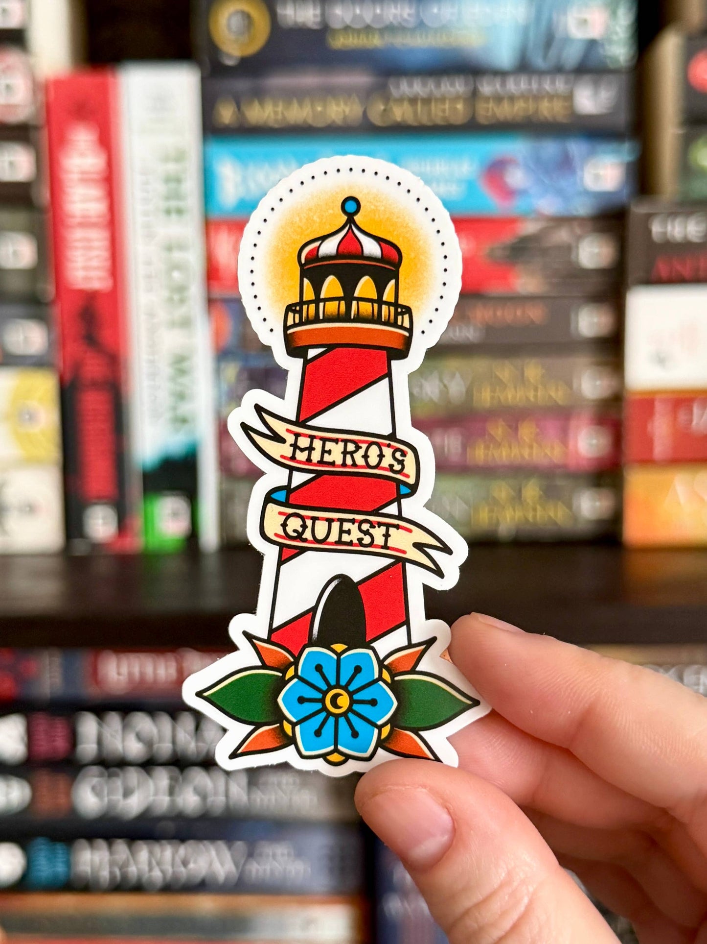 Sticker with 'Hero's Quest' design held in front of a bookshelf