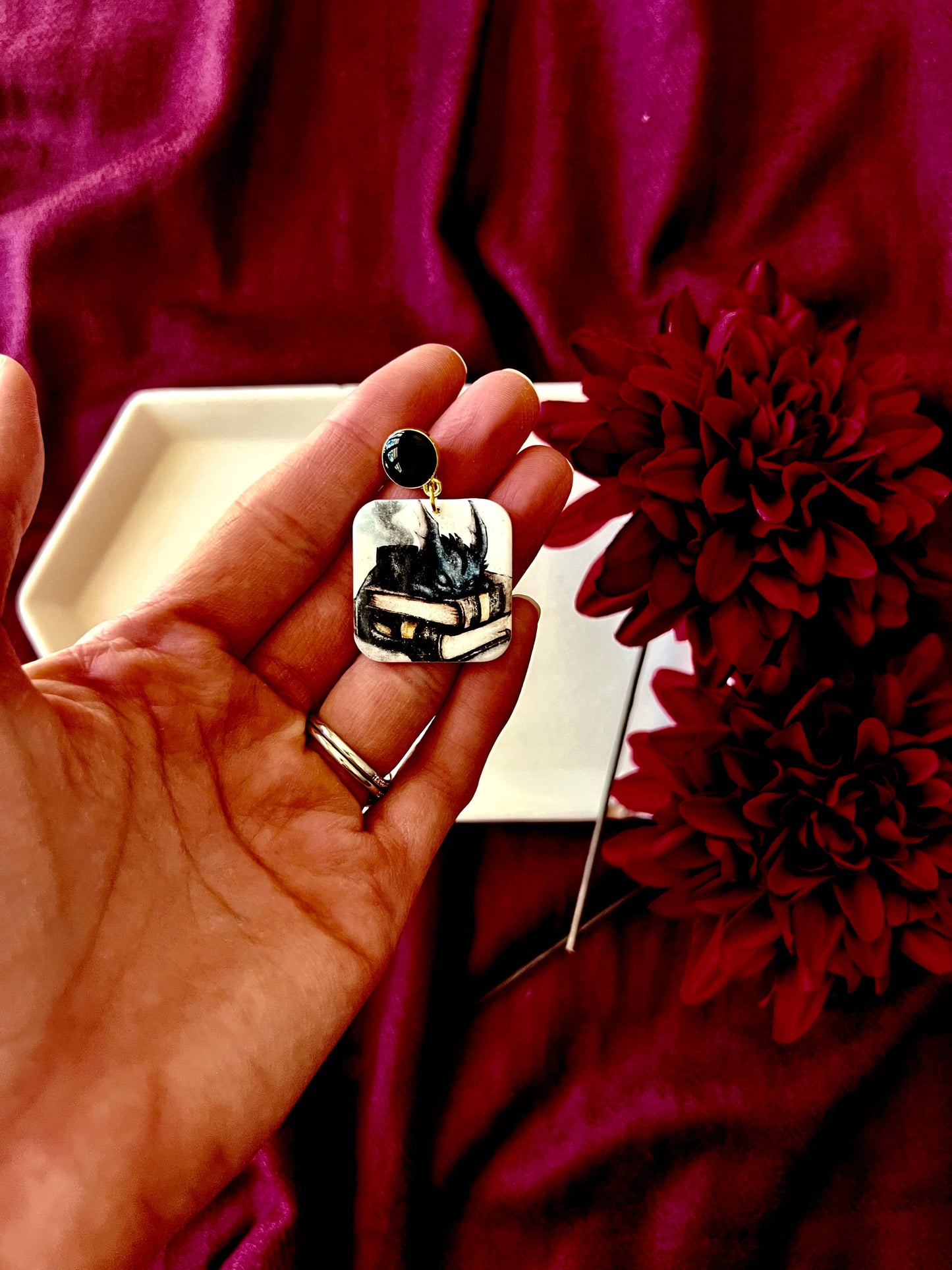 Hand holding a decorative earring with a piano design against a red background