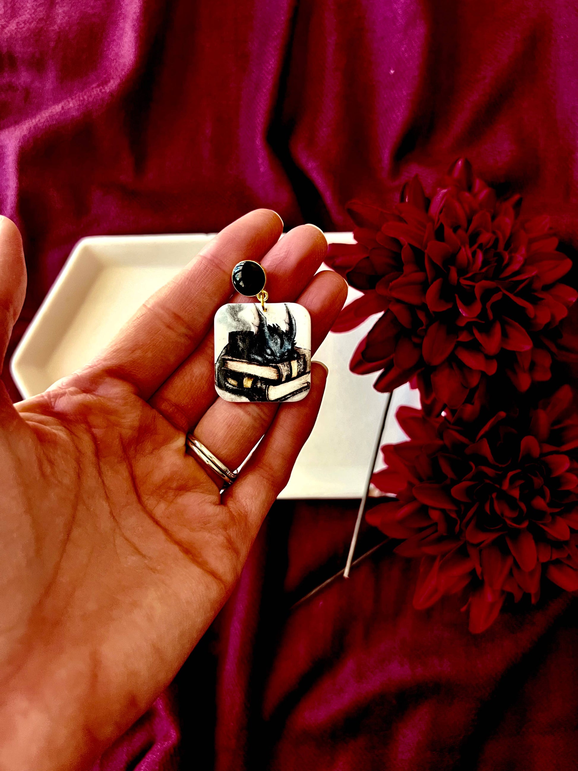 Hand holding a decorative earring with a piano design against a red background