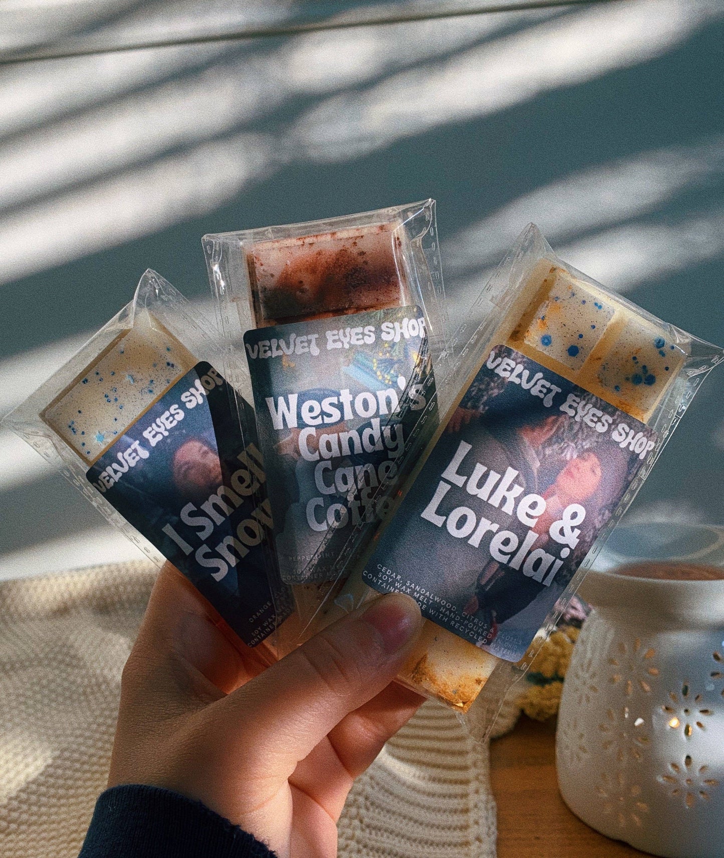 Hand holding three small candy packages with visible branding against a neutral background.