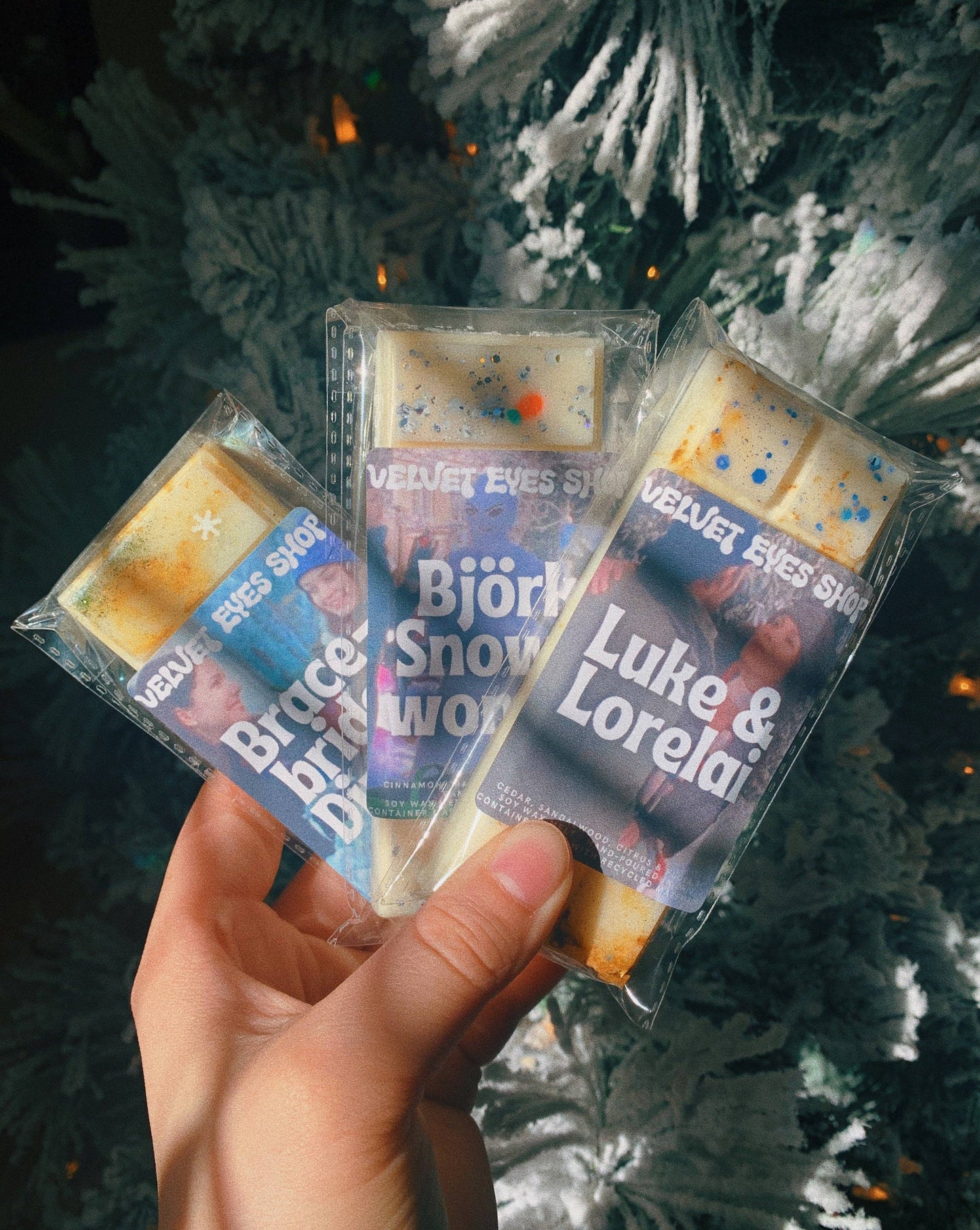 Hand holding three small packages with text in front of a Christmas tree.