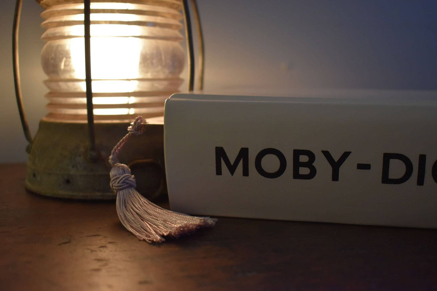 Book titled 'Moby-Dick' with a tassel and a lit lantern in the background