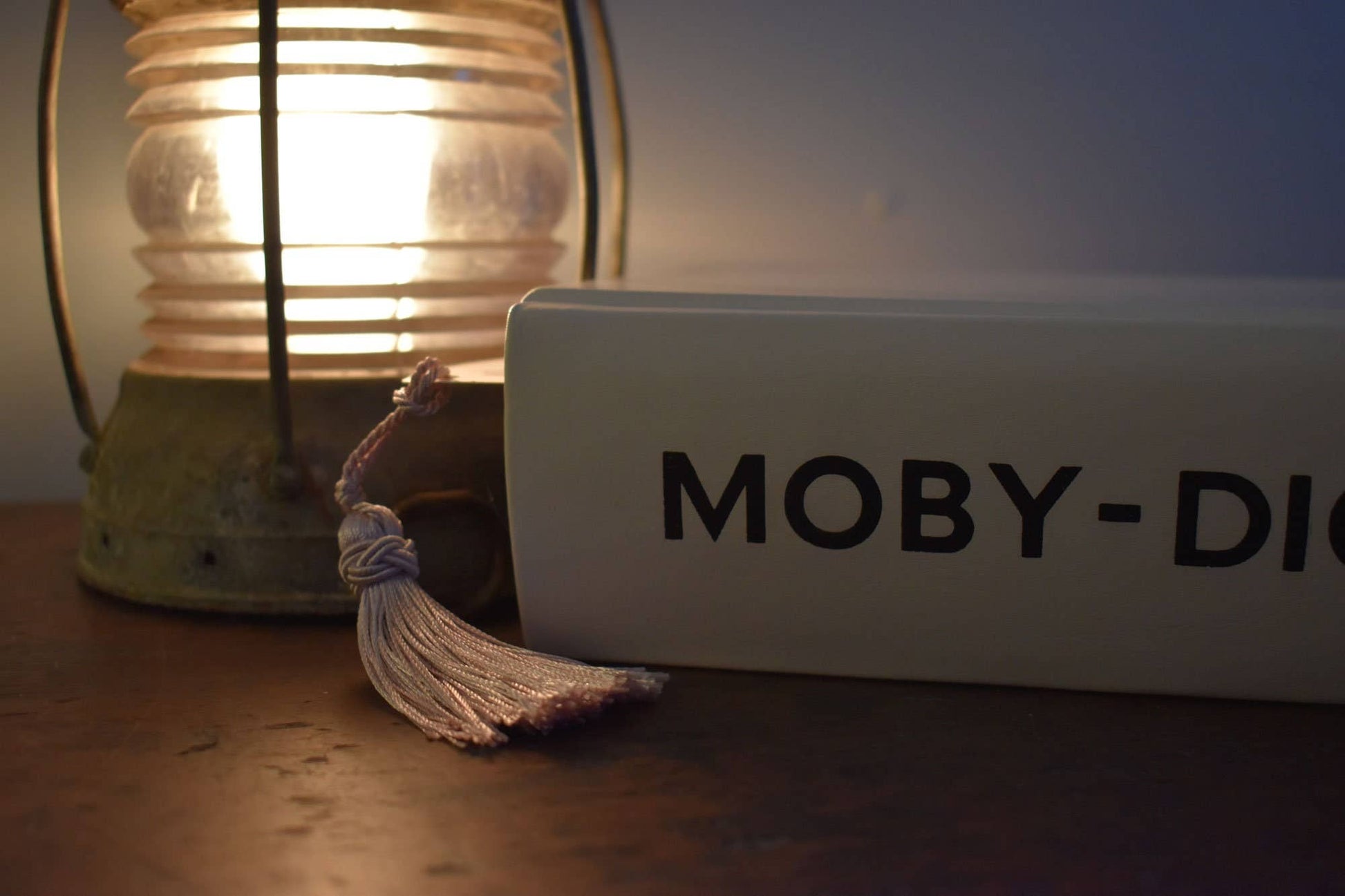 Book titled 'Moby-Dick' with a tassel and a lit lantern in the background