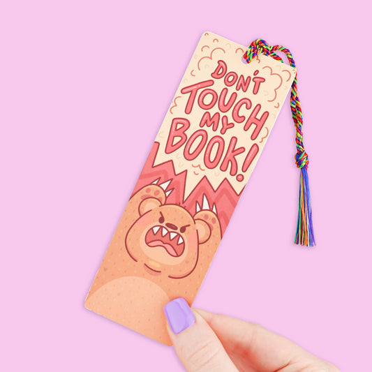 Bookmark with 'Don't Touch My Book!' text and tassel on a pink background
