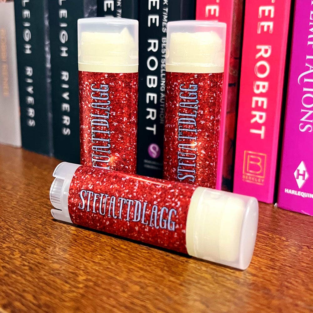 Red glittery lip balms with 'Stevattedlagg' branding on a wooden surface with books in the background.