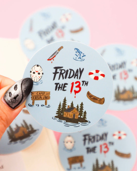 Sticker with 'Friday the 13th' theme held by a hand on a pink background