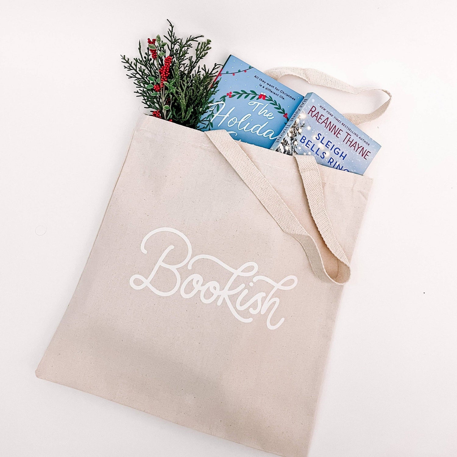 Beige tote bag with 'Bookish' text, filled with books and greenery on a white background
