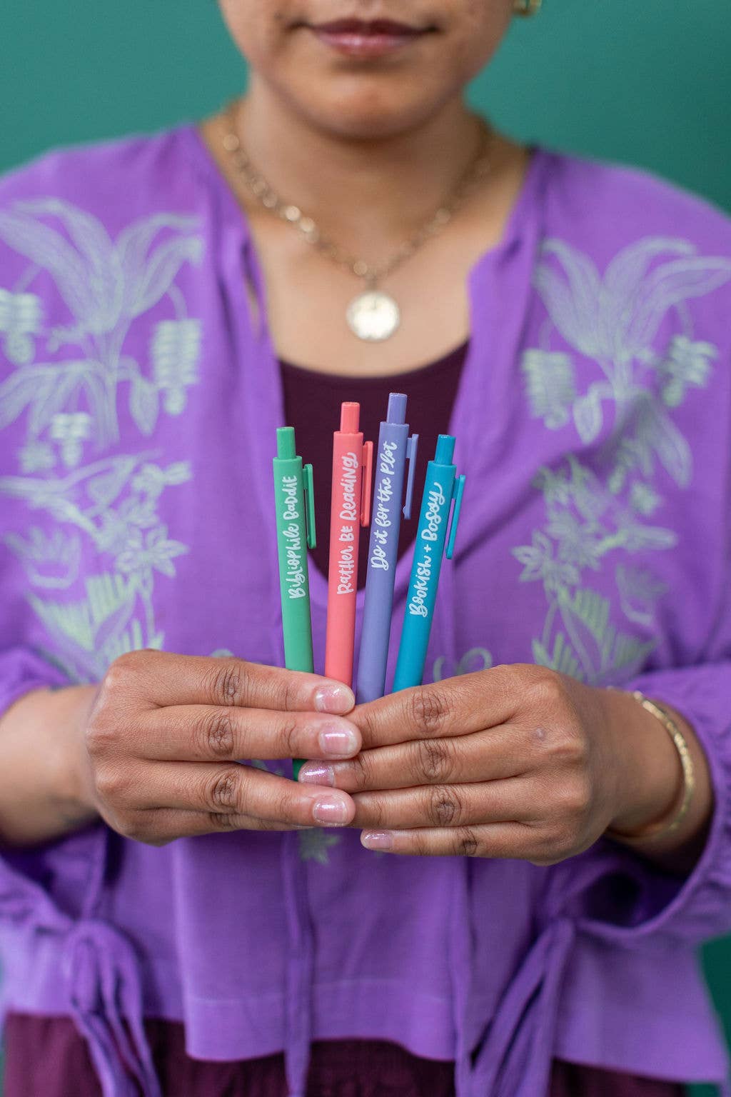 Person holding colorful pens with visible text against a green background
