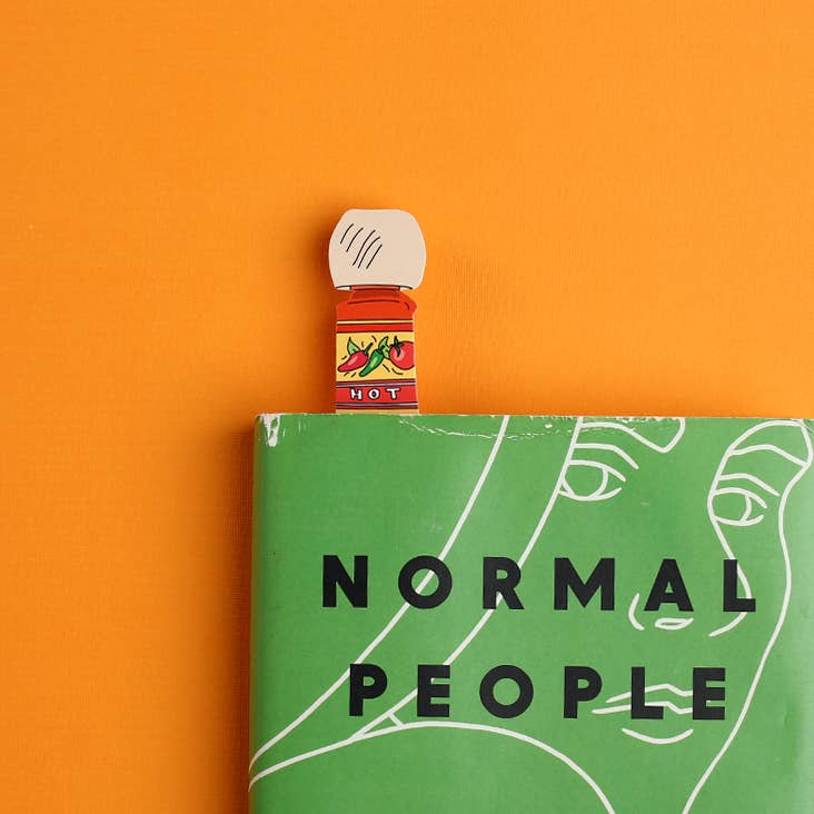 Small bottle of hot sauce on a book titled 'Normal People' against an orange background