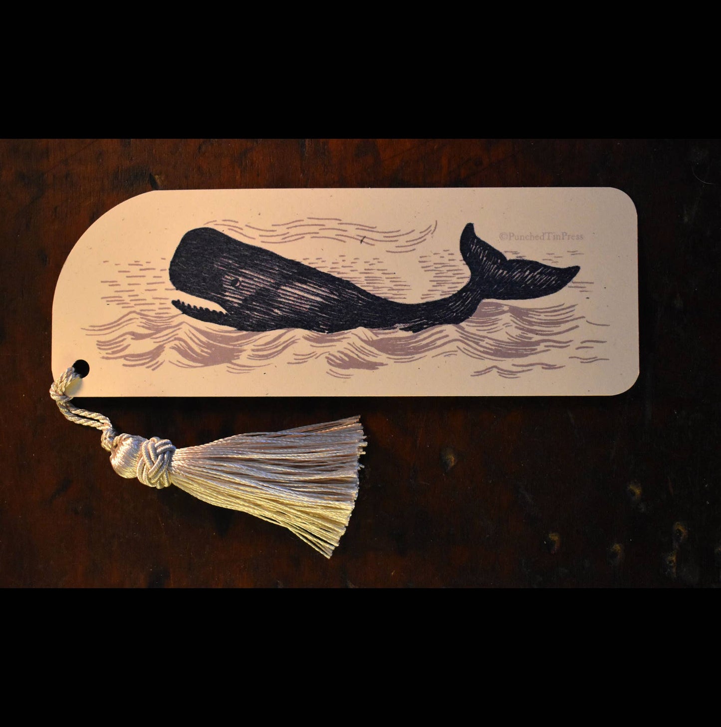 Bookmark with whale design and tassel on a wooden surface