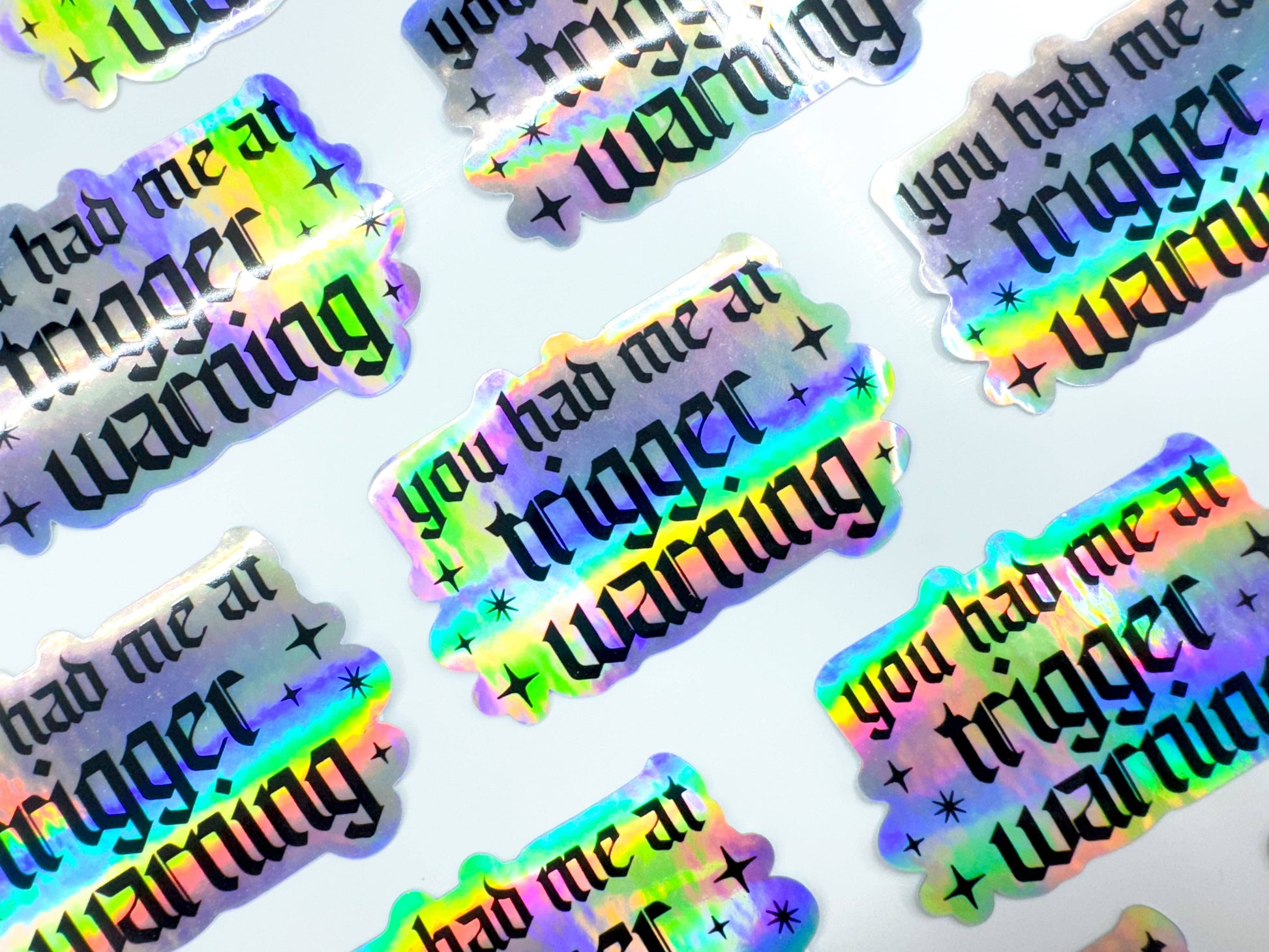 Holographic stickers with 'you had me at trigger warning' text on a white background
