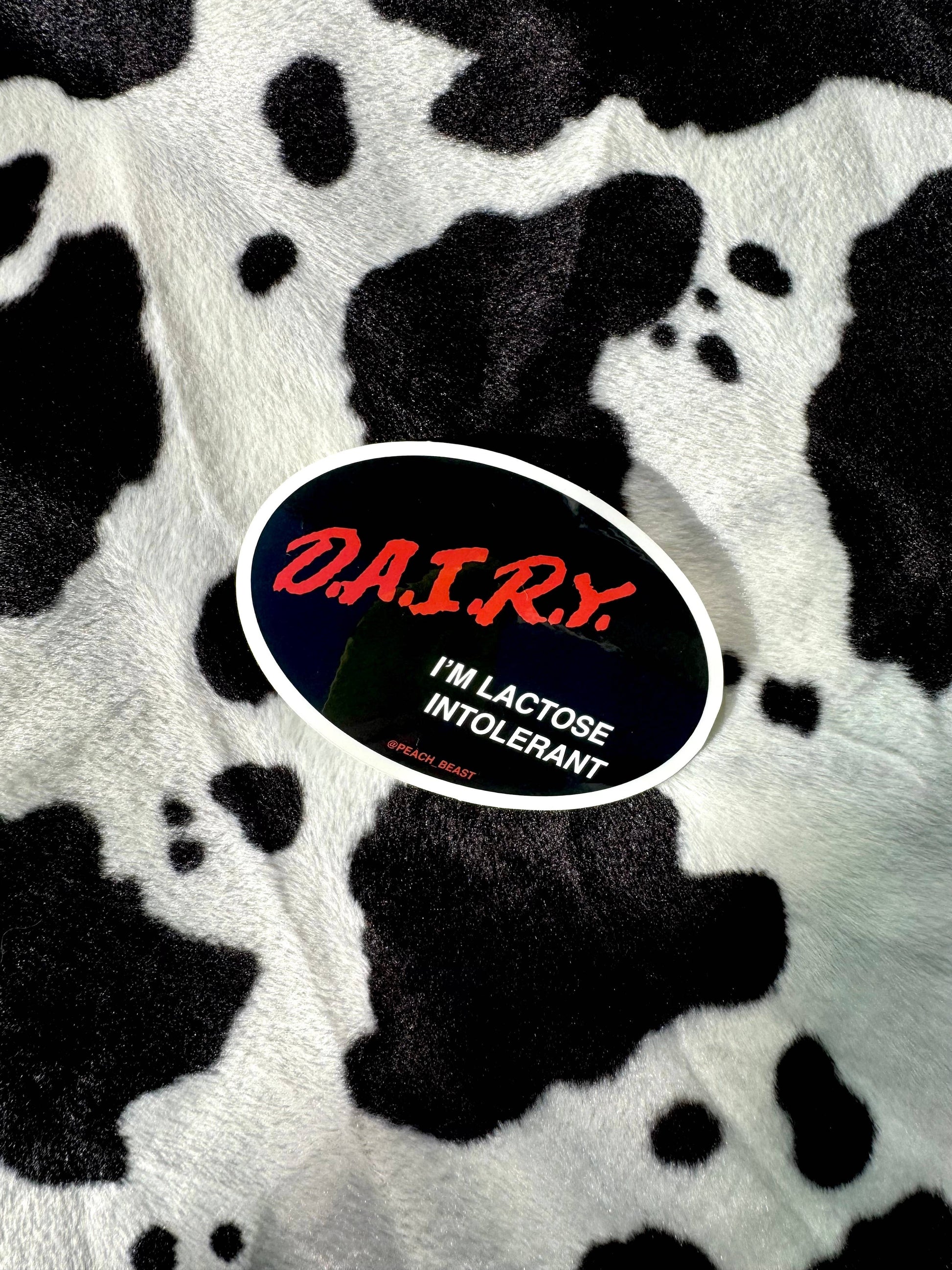 Sticker with 'DA.I.R.Y. I'M LACTOSE INTOLERANT' text on a cow print background