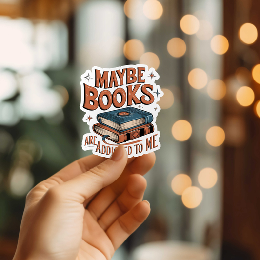 Hand holding a sticker with 'Maybe books are addicted to me' text against a blurred bokeh background