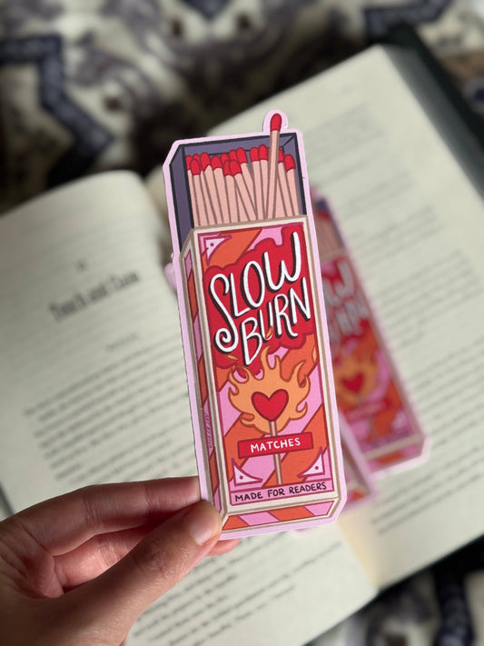 Box of matches labeled 'Slow Burn' held by a hand on a book background