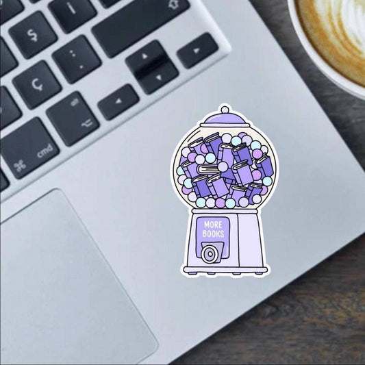 Laptop with a sticker of a gumball machine filled with books on a desk with a coffee cup.