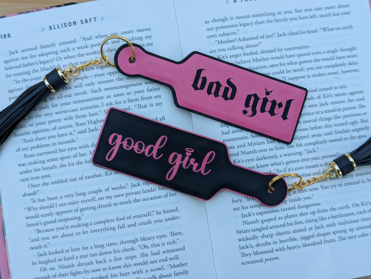 Two paddle-shaped keychains labeled 'bad girl' and 'good girl' on a book page.