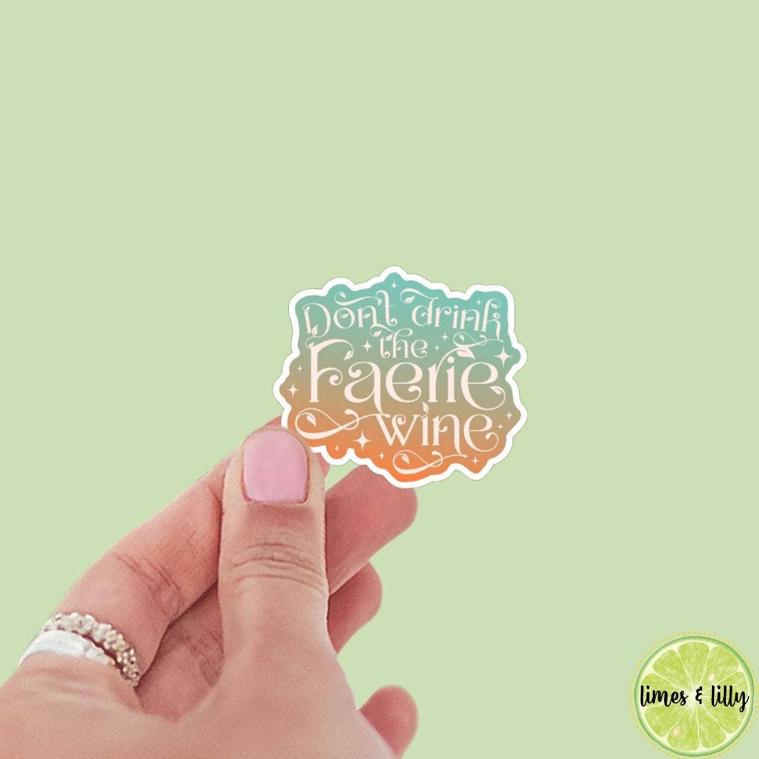 Hand holding a sticker with 'Don't drink the faerie wine' text against a light green background