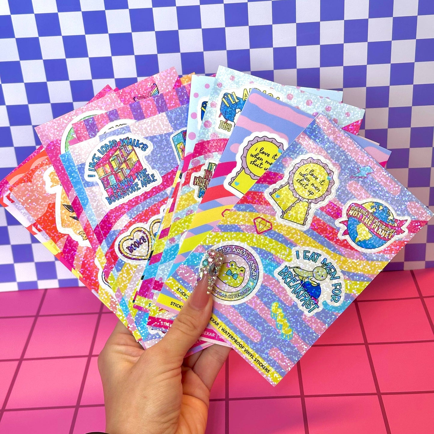 Colorful sticker sheets held by a hand on a checkered background