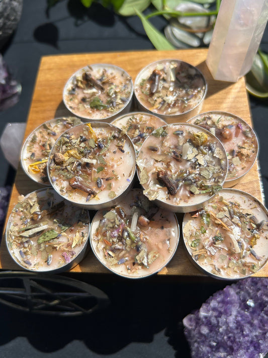 Small candles with herbs on a wooden board, surrounded by crystals.