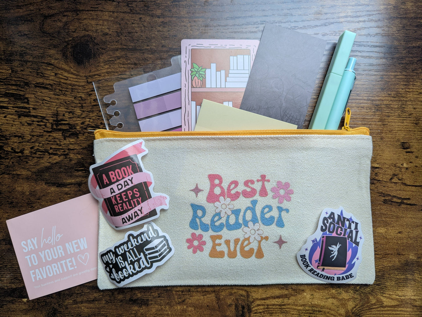 Pouch with 'Best Reader Ever' text, surrounded by books and stationery on a wooden surface