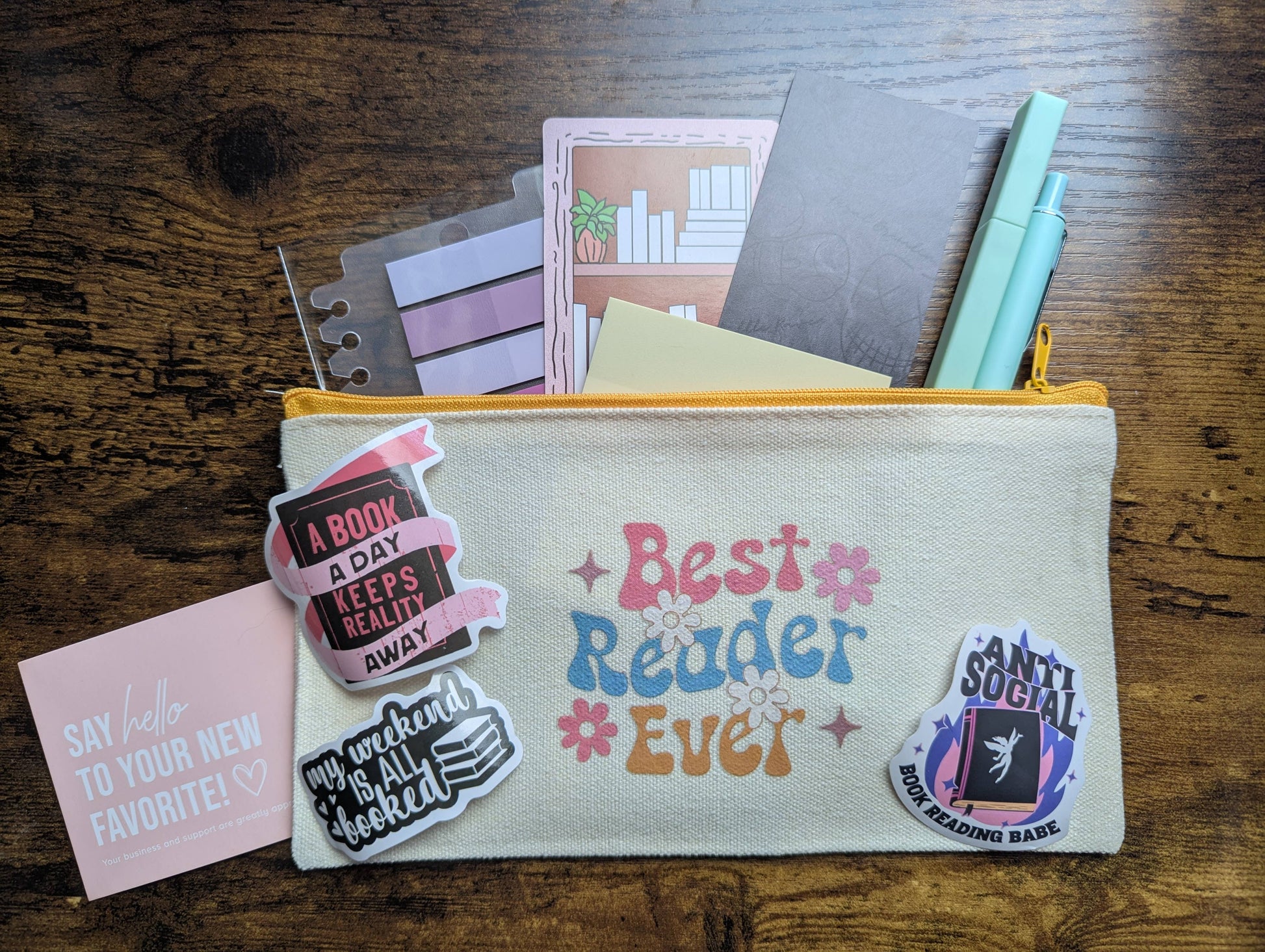 Pouch with 'Best Reader Ever' text, surrounded by books and stationery on a wooden surface