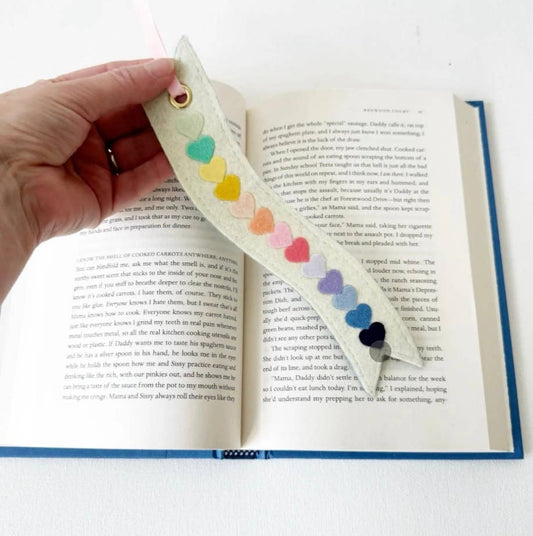 Hand holding a colorful heart-shaped felt bookmark on an open book
