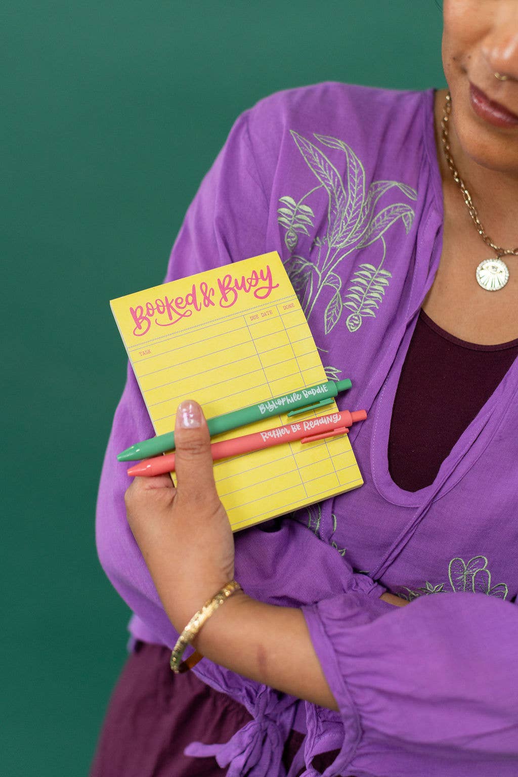Person holding a yellow notepad with colorful pens against a green background