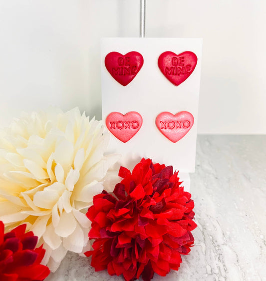 Red heart-shaped earrings on a card with flowers in the foreground