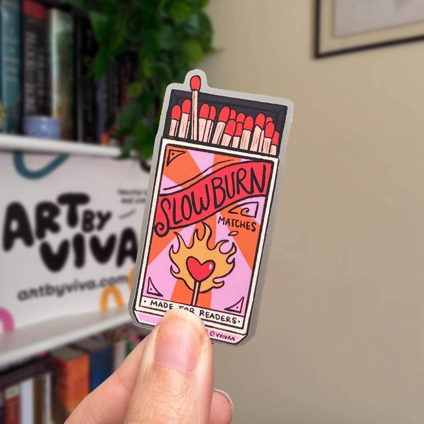 Sticker of a matchbox labeled 'Slow Burn Matches' held by a hand with a blurred background.