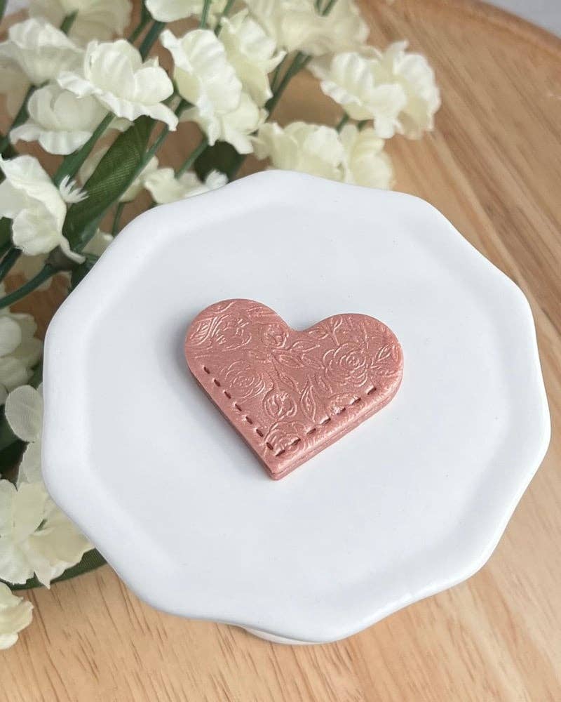Heart-shaped pink object on a white plate with flowers in the background