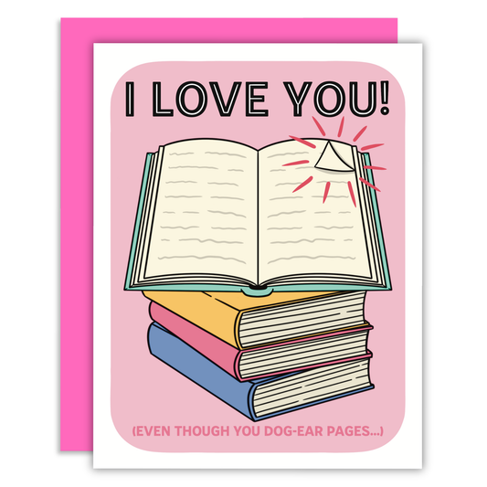 A greeting card with a pink envelope behind it. The card features a pink background with the text 'I LOVE YOU!' above an illustration of an open book resting on a stack of three closed books in yellow, pink, and blue.