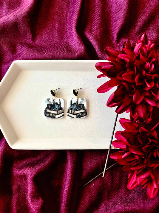 Pair of earrings on a white dish with a red flower on a purple fabric background