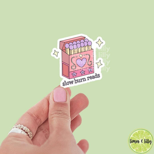 Pink matchbox with 'slow burn reads' text held by a hand on a light green background
