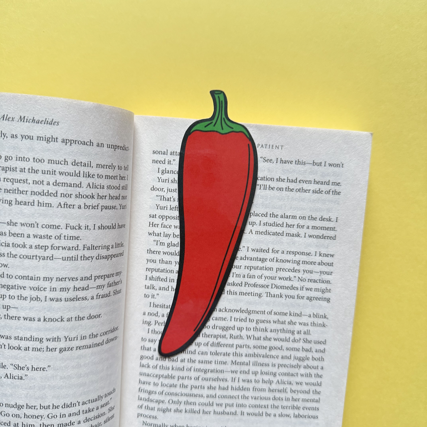 Red chili pepper-shaped bookmark on an open book with a yellow background