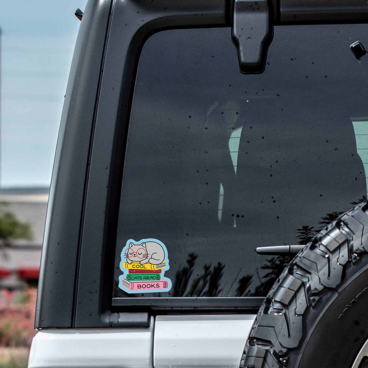 Car window with a sticker featuring a cartoon character and text, outdoors.
