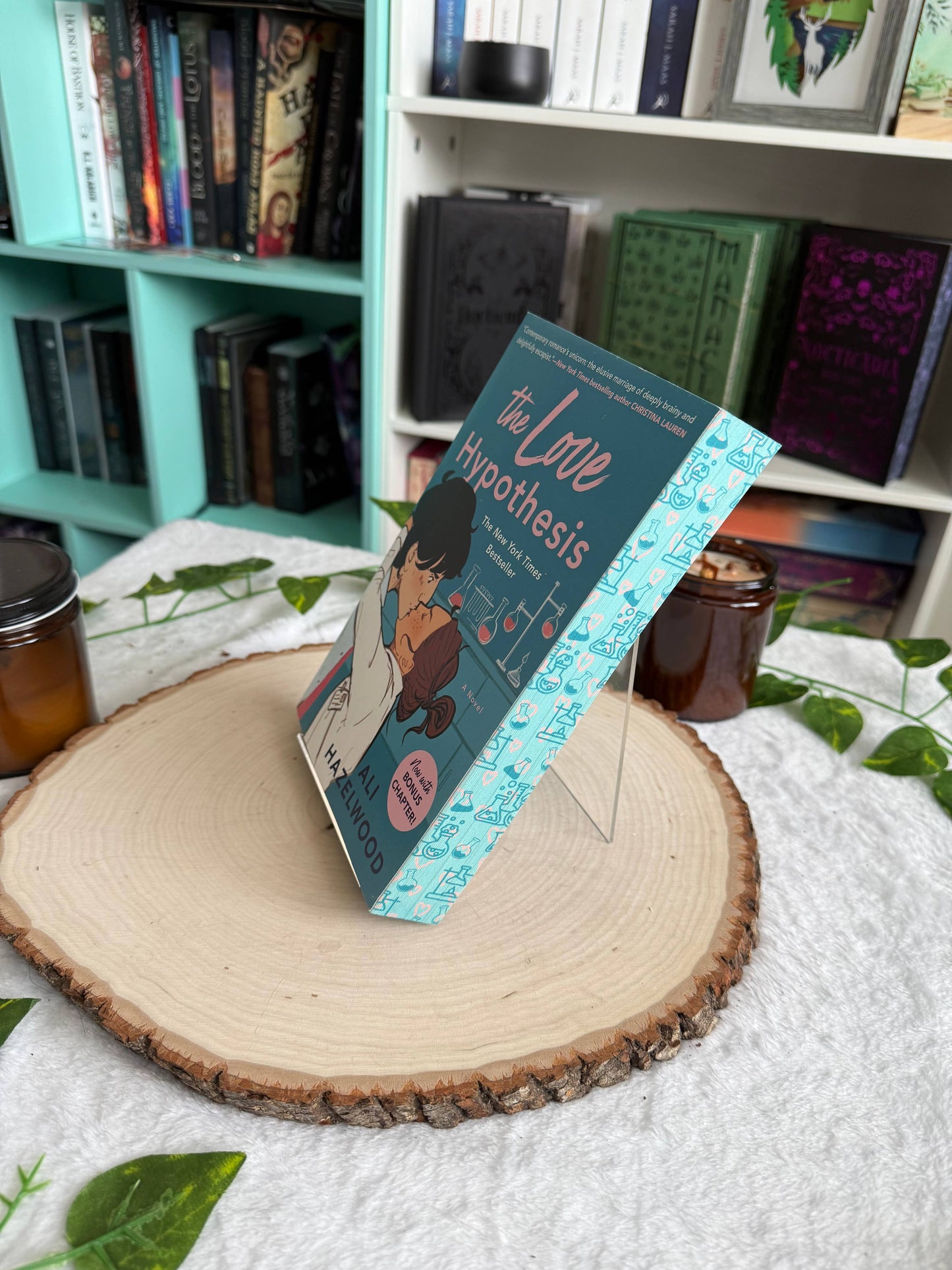 Book titled 'The Love Hypothesis' on a wooden stand with a bookshelf in the background