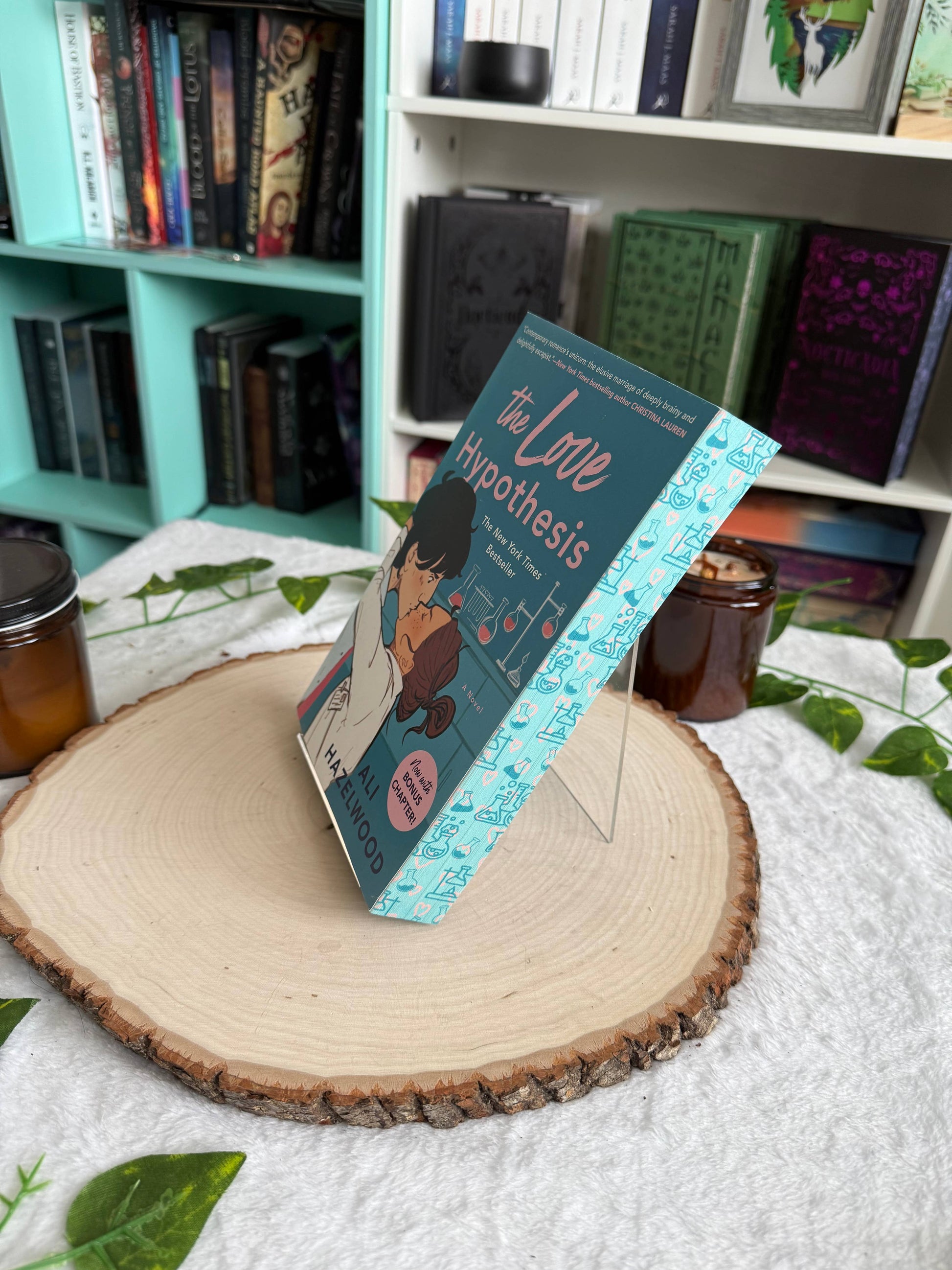 Book titled 'The Love Hypothesis' on a wooden stand with a bookshelf in the background