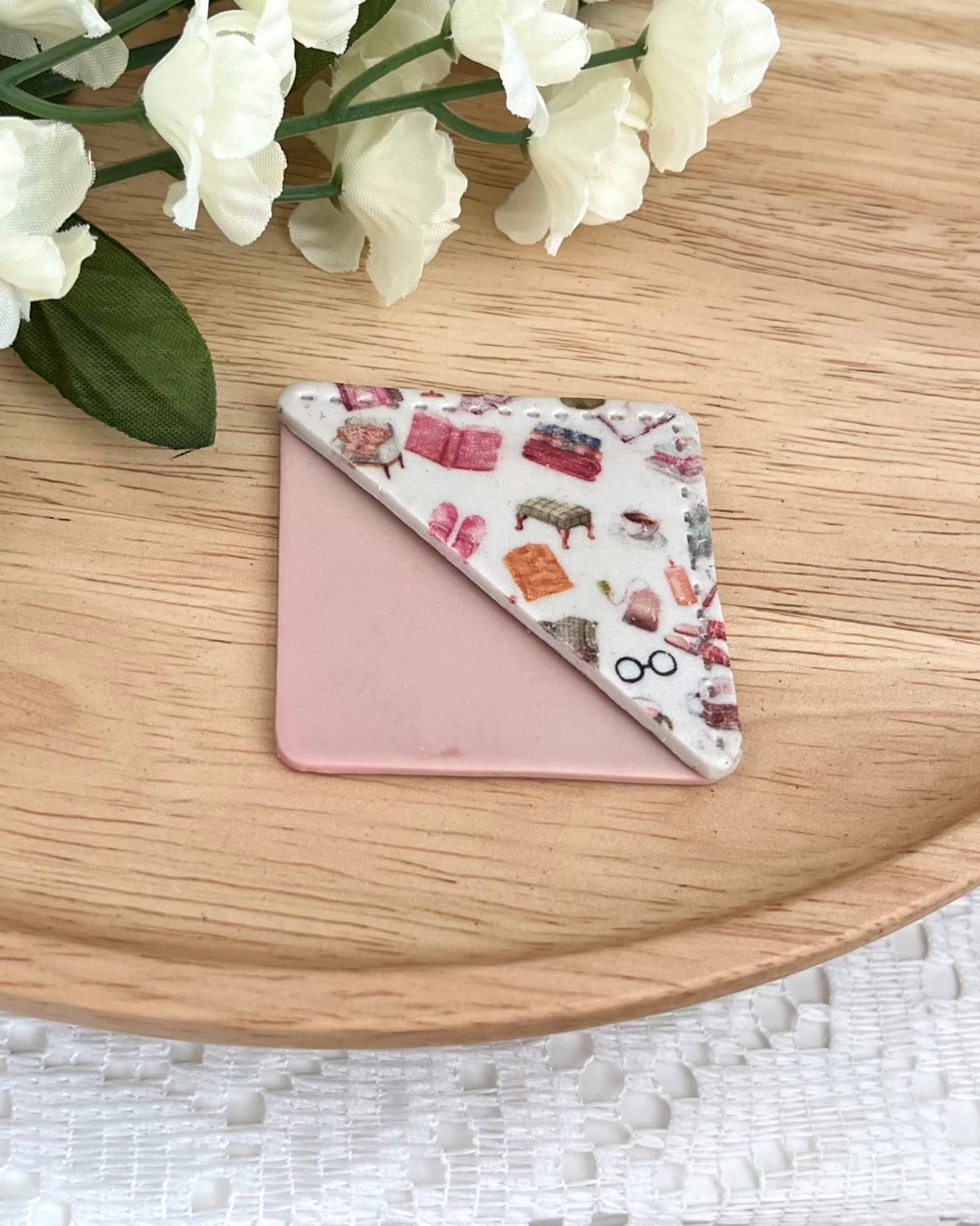 Small pink clay corner bookmark with a pattern on a wooden surface with white flowers.