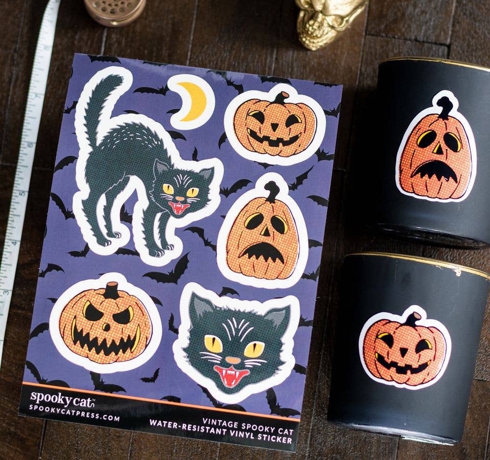 Vintage Halloween vinyl sticker sheet and matching candle decals featuring a black spookier cat and orange jack-o'-lantern pumpkins on a dark purple background, styled on a wooden surface with two black candles.