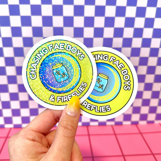 Two stickers with 'Chasing Fae Boys & Fireflies' text held against a checkered background.