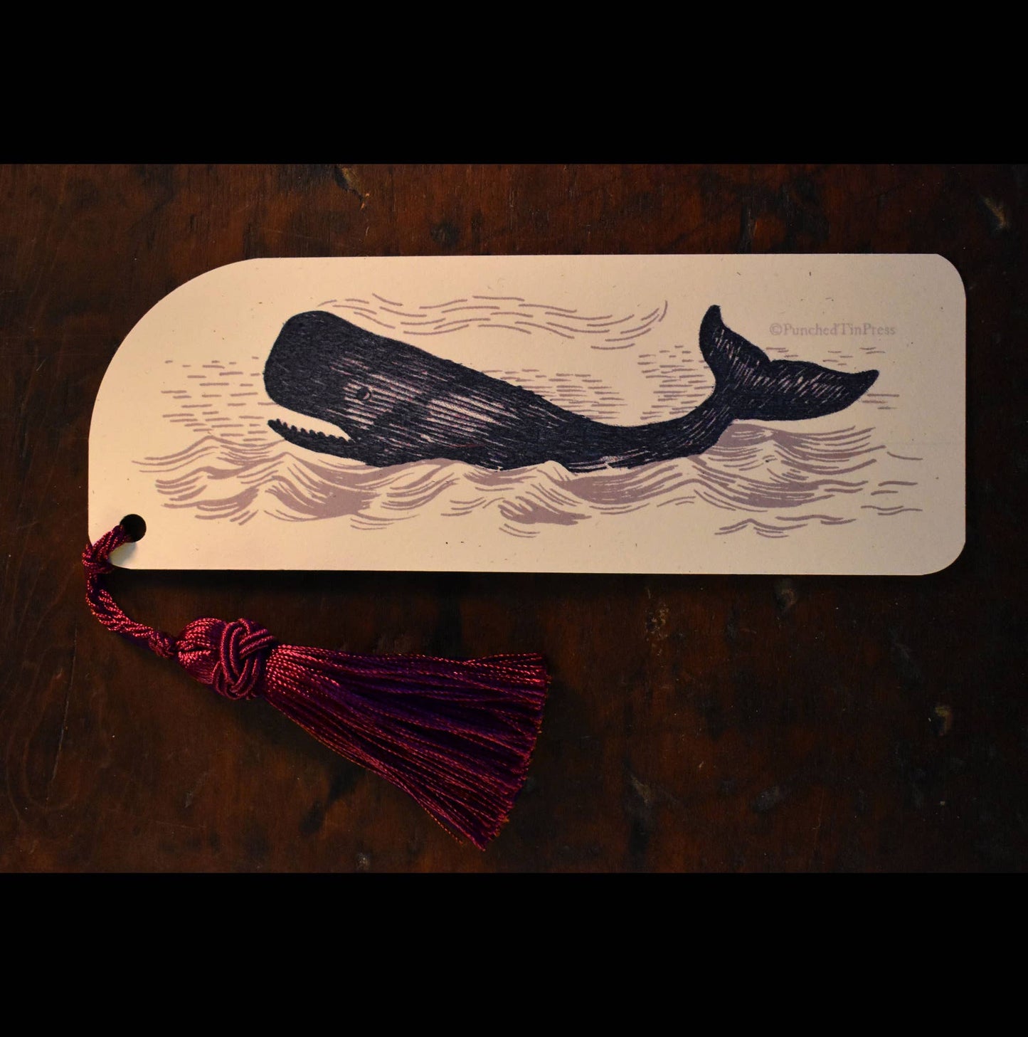 Bookmark with whale design and tassel on a wooden surface