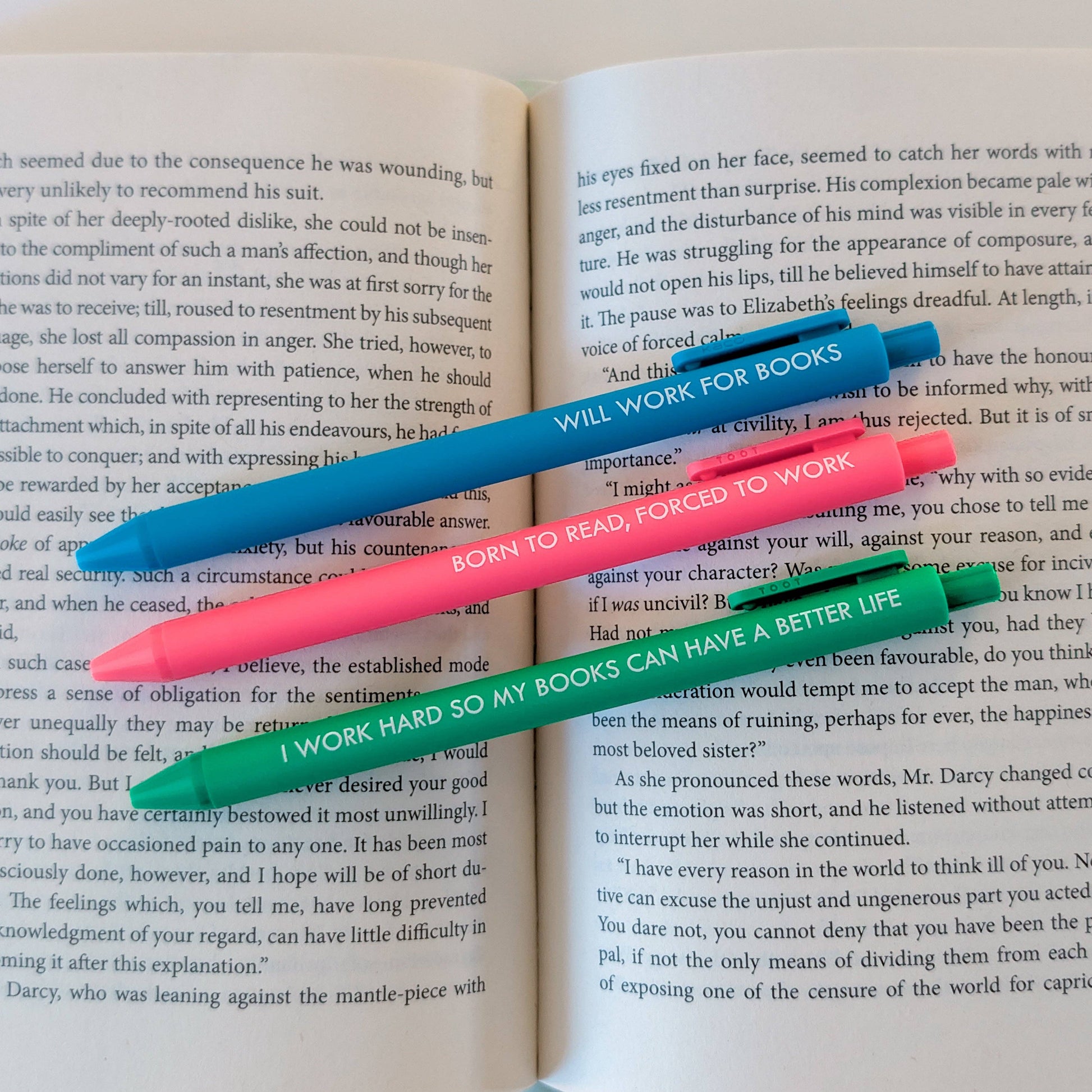Four colorful pens with humorous text on an open book
