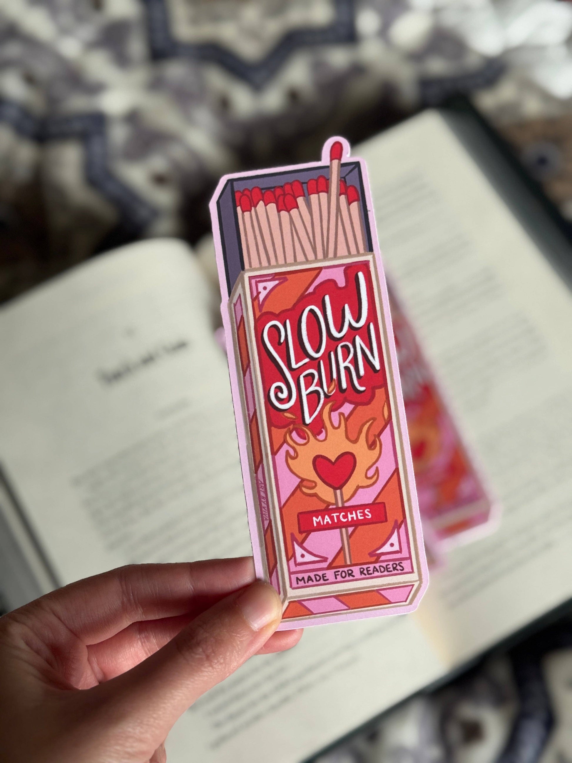 Box of matches labeled 'Slow Burn' held by a hand on a blurred background