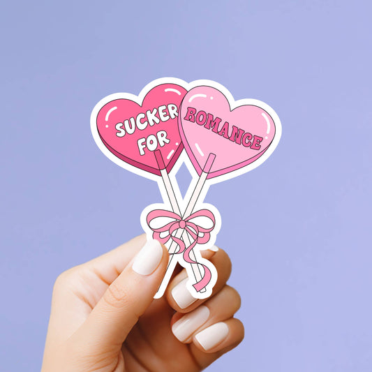Heart-shaped lollipops with 'Sucker for Romance' text held by a hand against a purple background