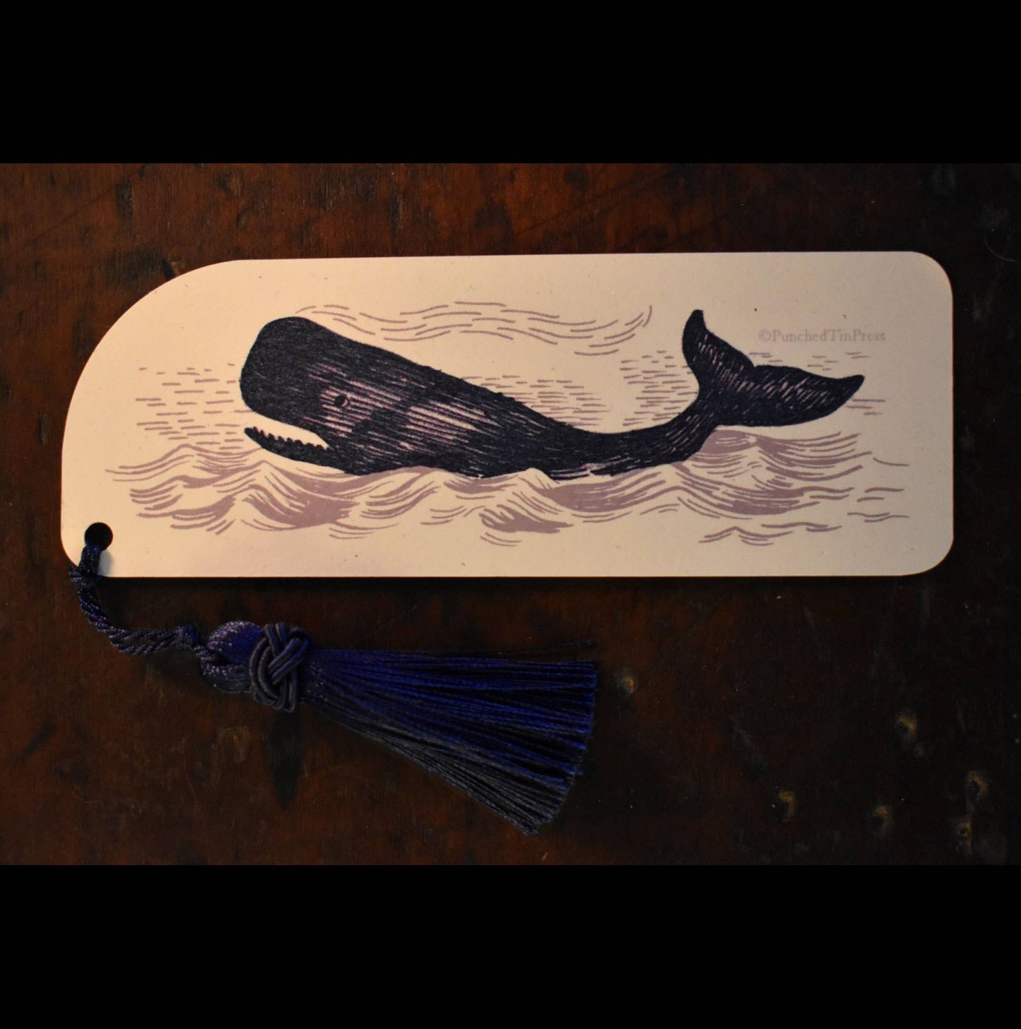 Wooden bookmark with whale design and tassel on a dark surface