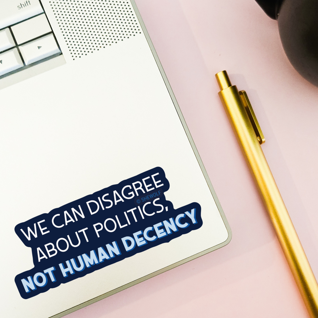 Notebook with a sticker reading 'We can disagree about politics, not human decency' on a desk with a pen and keyboard.