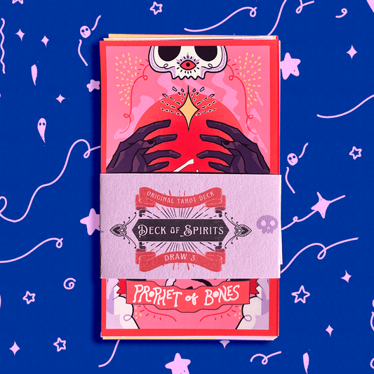 A boxed tarot deck wrapped in a paper sleeve labeled 'Deck of Spirits Draw 4' and 'Prophet of Bones,' shown against a bright blue background with pink doodled stars and abstract line art.