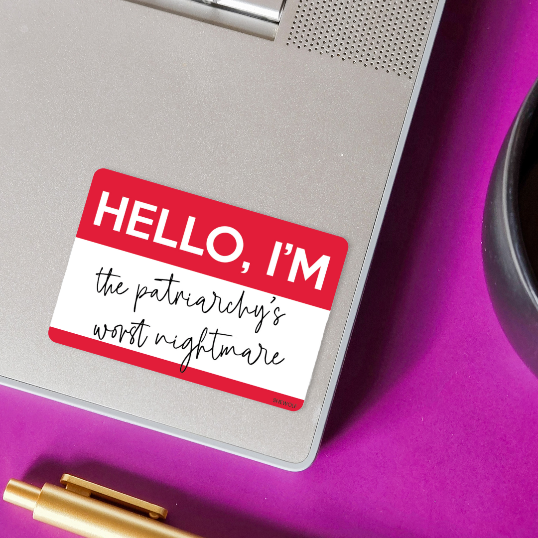 Notebook with a sticker reading 'HELLO, I'M the patriarchy's worst nightmare' on a purple surface.