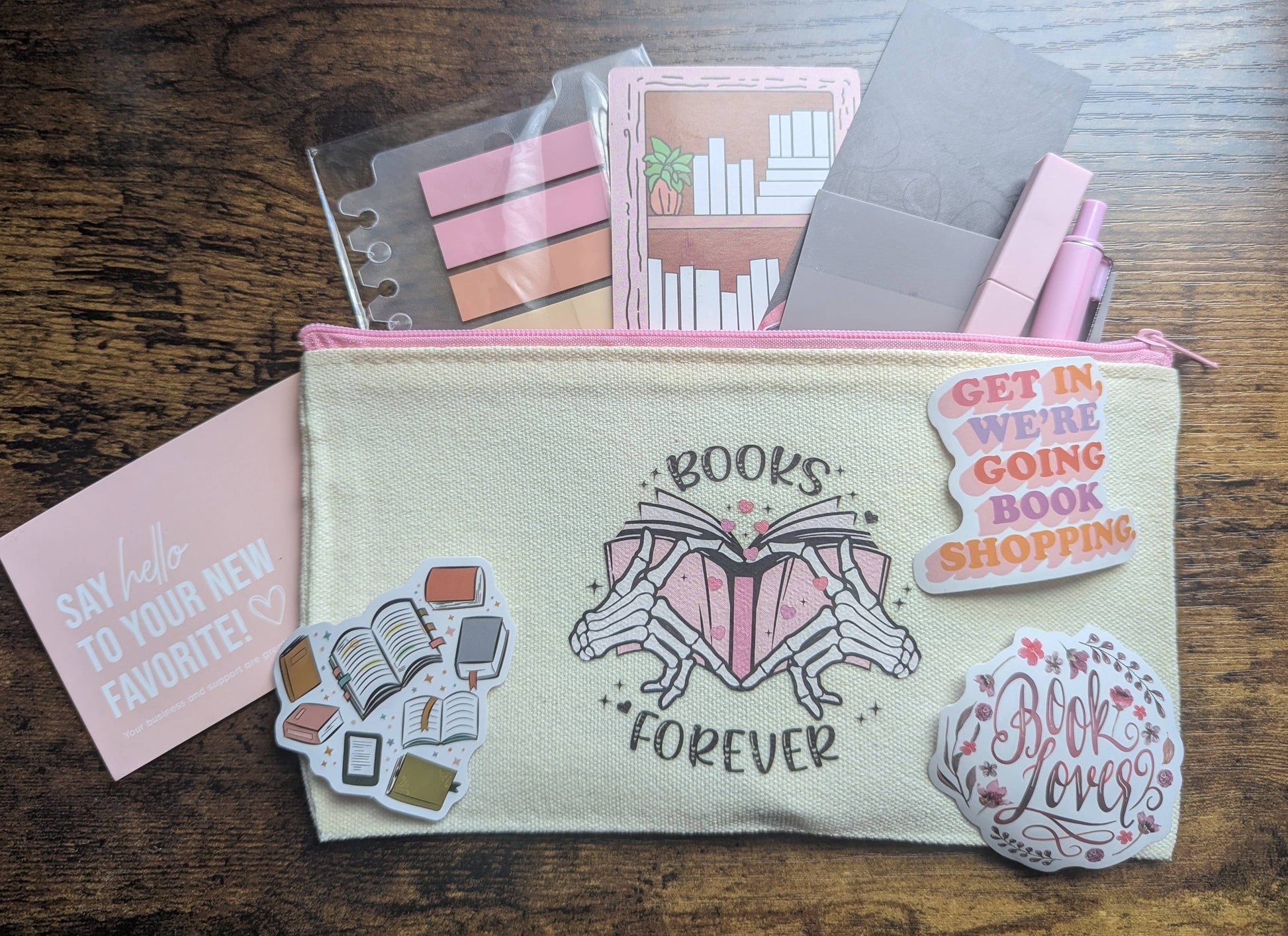 Pouch with 'Books Forever' design surrounded by stationery items on a wooden surface